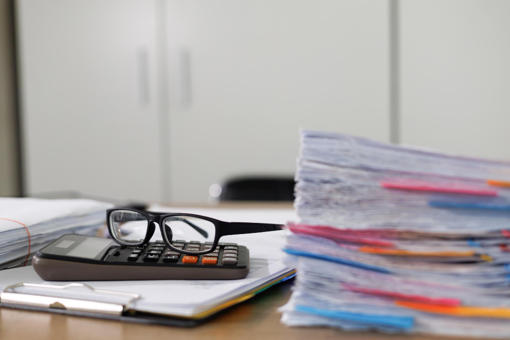 Stack of financial paperwork with a calculator and glasses